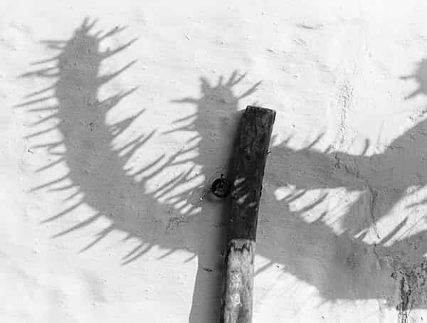 Es ist wie eine mikroskopische Aufnahme; inmitten von Schnee mit Textur steckt ein Pfahl, der mit einer Schleife aus einem roten Plastikstreifen versehen ist. Die rote Plastikschleife ist so gebunden, das ein auf dem Kopf stehendes V zu sehen ist - das ist alles.