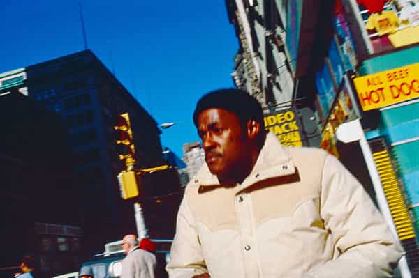 New York City im Februar 1982. Das satte Blau des New Yorker Himmels sticht hervor. In ihm eingebettet die prallen Farben der Werbeflaechen – HOT DOG – All BEEF -  des Big Apple. Ein zufaellig vorbeieilender Mann mit ernstem Gesicht, die Muetze auf, dicke Jacke, es ist noch kalt in der amerikanischen Metropole, man packt sich dick ein. Geschaeftigkeit und auch ein Hauch vertiefter Traurigkeit liegt in seinem Gesicht. Auch die Haerte und Kantigkeit, die ein Leben in dieser Stadt mit sich bringt.  Und gleichzeitig: Ein heimlicher, in Schnappschussaufnahme eingefangener Blick in die Ferne, die nur in den langen, breiten Straßen der Stadt wieder zu finden ist.