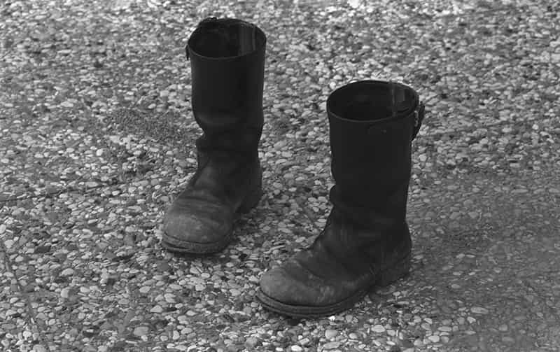 Ein Paar schwarze halbhohe Stiefel stehen auf Waschbetonplatten. Die Schuhsohlen loesen sich an der Spitze ab. Es ist eine Schwarzweiss Fotografie.
