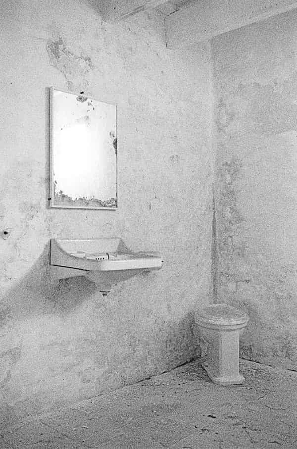 Der Dachboden einer verlassenen Finca auf Menorca. Nur in der Mitte des Dachstuhls ist er begehbar. Ein edles helles Grau ist die vorherrschende Farbe dieser S/W - Fotografie. Ein Teil des gekaelkten hoelzernen Dachstuhls ist im rechten Teil der Fotografie zu sehen. Zwei Fenster sind in der Giebelwand eingelassen, eines links und eines rechts Im Bild. Die Aussenwelt nimmt man nur diffus war, dafuer stroemt das Sonnenlicht von schraeg links in den Raum. Die rechten Wangen der glaslosen Fensteroeffnungen gleissen. Die Fenster begrenzen das Licht und finden sich auf dem Boden des Daches in Form eines Rechtecks illuminiert abgebildet wieder. Der Boden ist mit Staub ueberdeckt, ein wenig Unrat ist zu sehen.