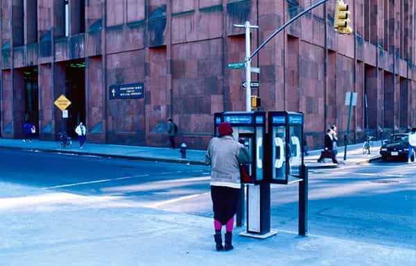 Wieder New York, 80er Jahre. Plastisch, kuehl, grafisch - eine Momentaufnahme einer Kreuzung an der Washington Street. Im Hintergrund ein schon in die Jahre gekommenes typisches New Yorker Buerogebaeude – seine Groeße laesst sich nur erahnen. Das Gebaeude erinnert an die Klasse des jungen Art-Deko-Stils der aufstrebenden Finanzmetropole - es huellt sich mittlerweile in einen dem Dampf und dem Smog geschuldeten morbiden Charme. Ein Moment der Privatheit in der Mitte des Bildes: eine Frau spricht an einem öffentlichen Telefon, ihre pinken Strumpfhosen geben der Szene seine Verspieltheit zurueck. Auch die Verspieltheit der Telefonicons auf dem Telephone Booth a la 80er Jahre verleihen dem Bild ein Augenzwinkern. Was nicht fehlen darf in der New Yorker Szenerie: die vorbeieilenden Geschaeftsleute mit ihrer taeglichen Determiniertheit und Geschaeftigkeit. Und wie immer, das Gelb der Ampelsteelen, die den Kontrast zur blauen winterlichen Kaelte des Fotos darbieten.